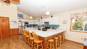 A kitchen with a large island, wooden chairs, and bar stools. - Oceanside, Private Pool, Hot Tub, OS4N, Kaerolla Dawn (Corolla)