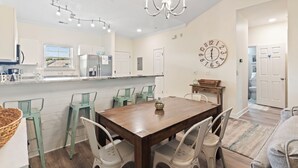 A modern kitchen with white cabinets, a wooden dining table, and green chairs.