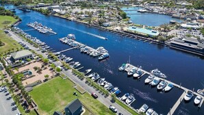An aerial view of a marina with numerous boats docked, a bridge, and surrounding buildings.