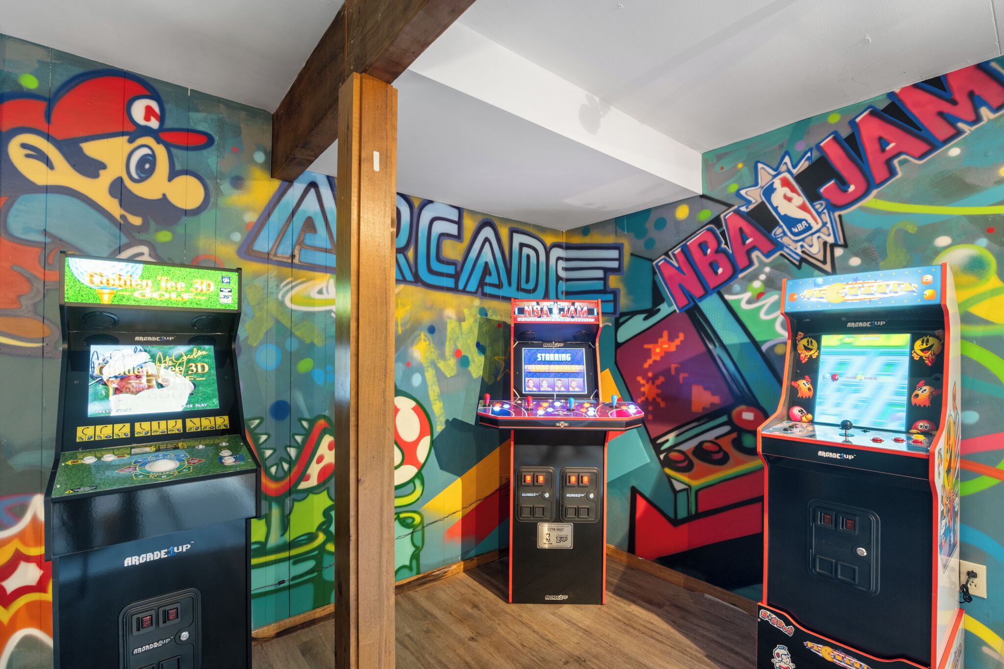 A room with arcade machines, colorful murals, and wooden beams.