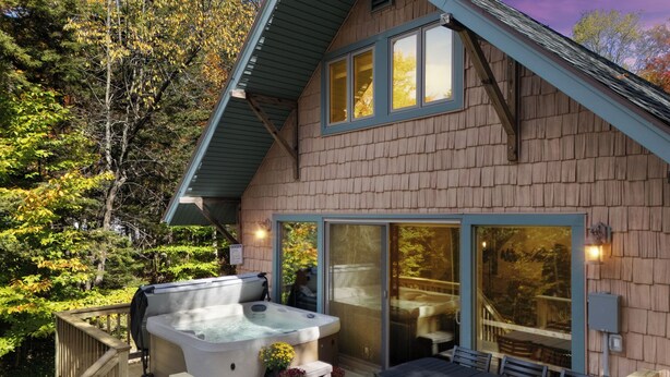 A wooden cabin with a hot tub, outdoor seating, and a deck.