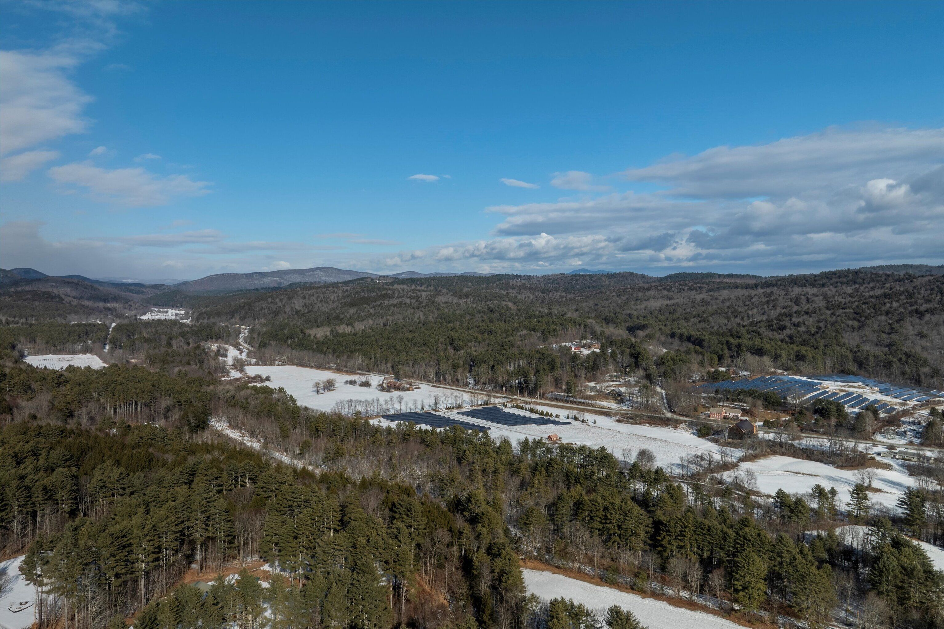 A panoramic view of a mountainous area with a mix of forested and open spaces, including a large building complex with solar panels.