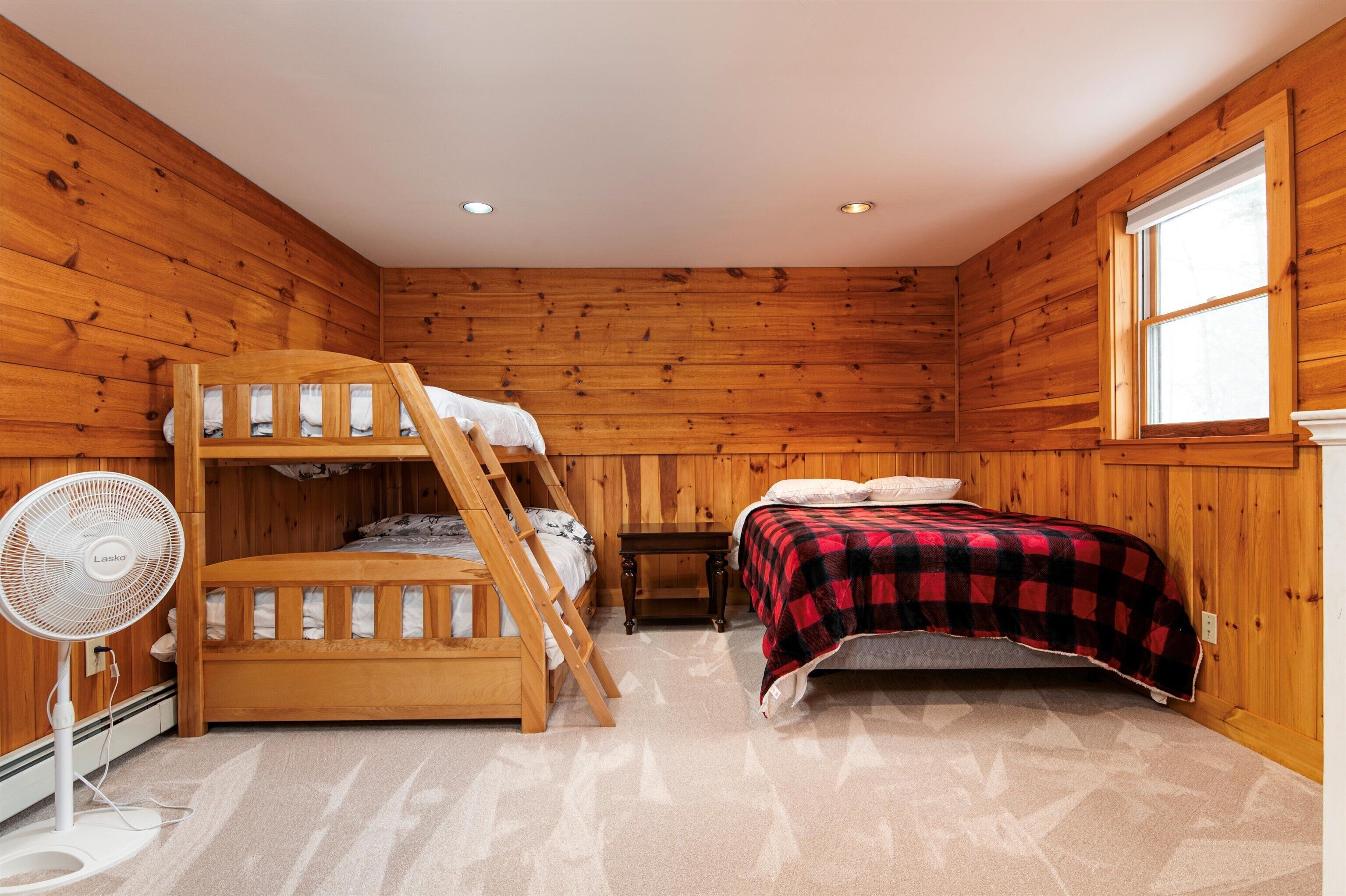 A bunk bed room with a fan, a window, and wooden walls.