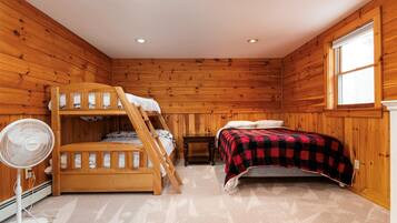 A bunk bed room with a fan, a window, and wooden walls.