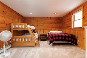 A bunk bed room with a fan, a window, and wooden walls.
