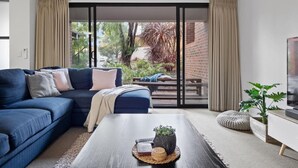A modern living room with a blue sofa, a coffee table with a plant, and a sliding glass door leading to a garden.