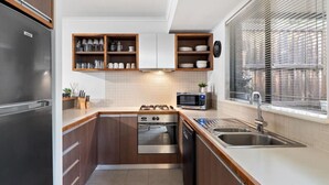 A compact kitchen with wooden cabinets, a stainless steel refrigerator, a microwave, an oven, and a sink.