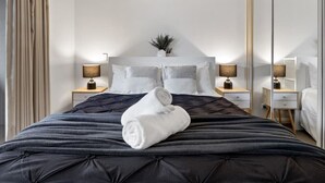 A neatly made bed with a black quilt, two bedside tables with lamps, a mirror, and a plant on the headboard.