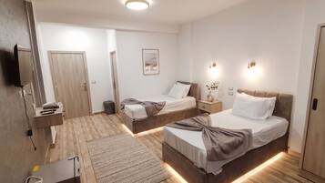 Une chambre d’hôtel moderne équipée de deux lits, d’un téléviseur à écran plat, d’une table de chevet, d’une poubelle et d’un luminaire fixé au mur.