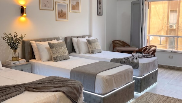 A modern bedroom with two beds, a bedside table with a lamp, framed artwork on the wall, and a window with an air conditioning unit. - Park Plaza hotel (Cairo)
