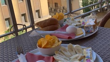 A balcony with a table set for breakfast, including bread, eggs, ham, and chips.
