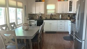 Eine Küche mit weißen Schränken, einem Esstisch mit Stühlen, einem Kühlschrank und einem Fenster mit Jalousien.