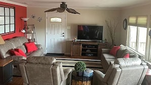 Ein Wohnzimmer mit einer Couch, Sesseln, einem Fernseher und einem Deckenventilator.
