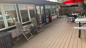 Eine überdachte Terrasse im Freien mit Holzboden, Metallstühlen, einem roten Sonnenschirm und einem Tisch.