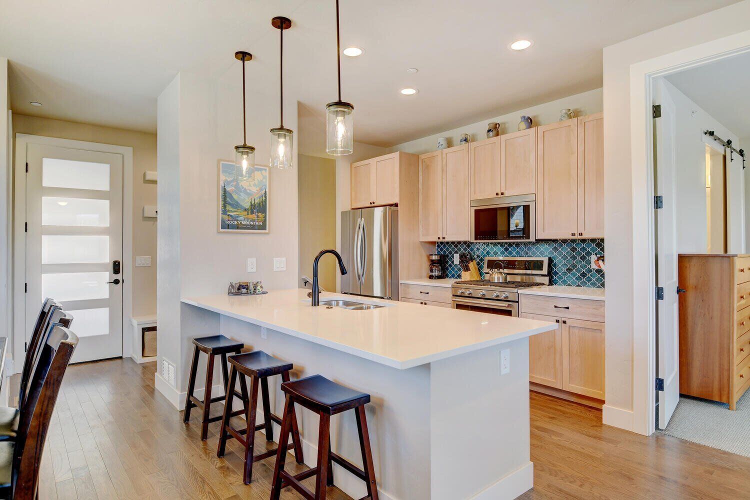 A modern kitchen with a central island, bar stools, stainless steel appliances, and pendant lighting.