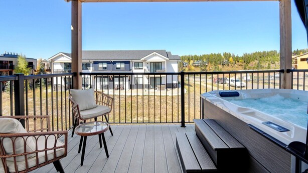 Un espacio exterior techado con un jacuzzi, sillas de mimbre y vistas a edificios residenciales.