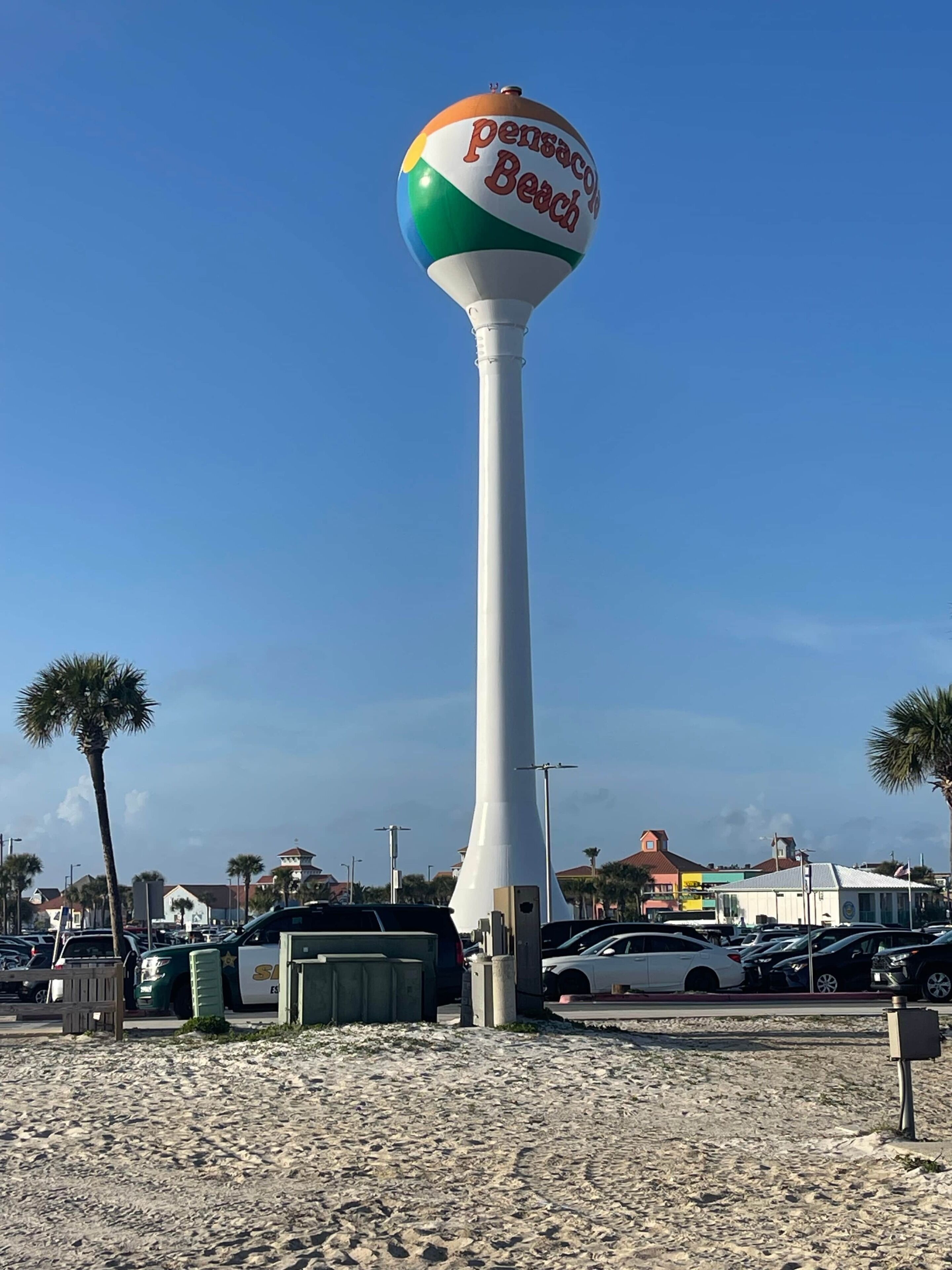 A tall white structure with a colorful beach-themed top, surrounded by a parking area and palm trees.