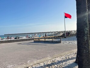 A beach with a wooden pier, a flag, and a stone wall.