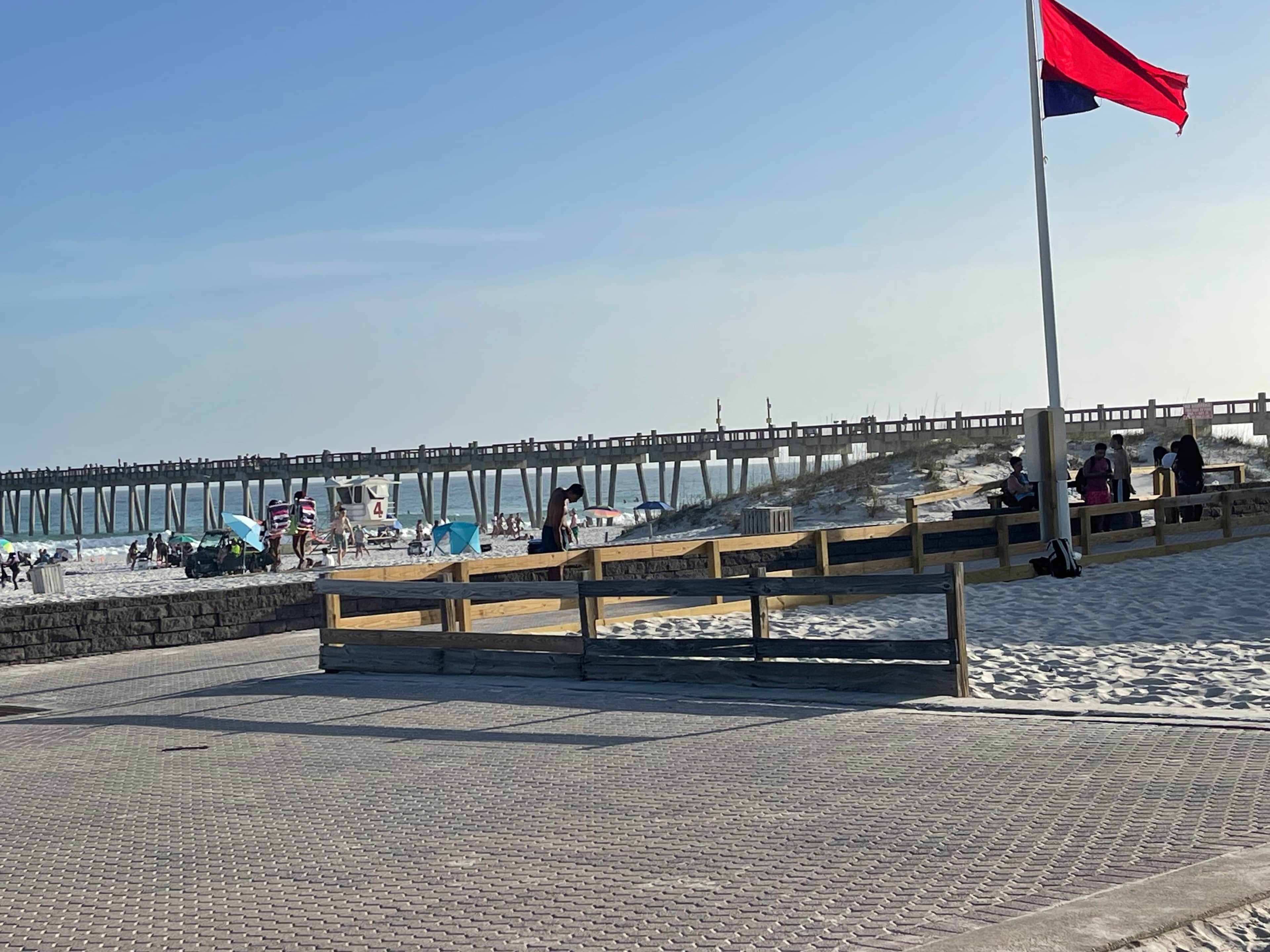 Een strand met een houten steiger, een vlag en mensen.