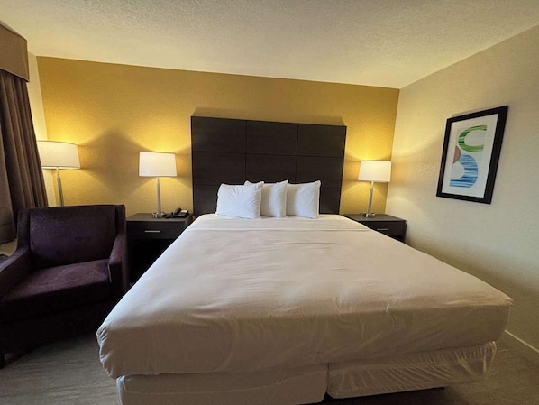 A hotel room with a large bed, two bedside tables, a chair, and a framed picture on the wall. - Studio 6 Suites Charlotte, NC - Northlake (Charlotte)