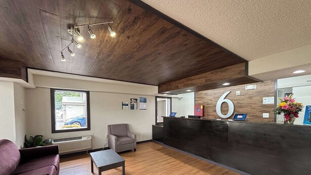 A reception area with a wooden floor, a reception desk, a grey armchair, a small table, and a window with a view of a building outside.