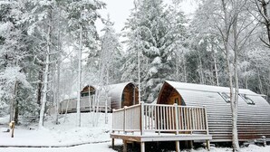A row of log cabins with wooden decks and railings, surrounded by snow-covered trees. - Cosy Couples Cabin in the Scottish Highlands (Tomintoul)