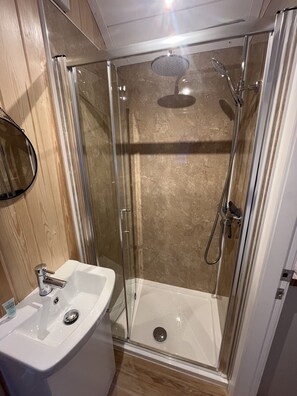 A shower with a glass door, a white sink, and a wooden wall. - Cosy Couples Cabin in the Scottish Highlands (Tomintoul)