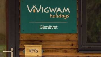 Eine Holzwand mit einem Schild, auf dem 'WIGWAM holidays Glenlivet' steht, und einem Kreideschild mit der Aufschrift 'WILLKOMMEN! BEI WIGWAM HOLIDAYS GLENLIVET!'.