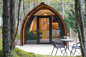 A cozy, wooden cabin with a glass door entrance, a small patio with two chairs, and a deck area. - Cosy Couples Cabin in the Scottish Highlands (Tomintoul)