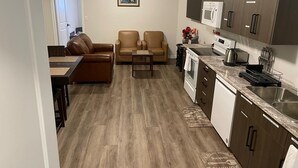 A compact kitchen with a microwave, toaster, and sink. There is a dining area with a brown leather couch and a small table. The floor has a wood-like pattern, and there is a framed picture on the wall. - Bright Private 2BR Suite | Near Niagara Falls | Family-Friendly (Pelham)