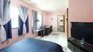 Een slaapkamer met een bed, een bureau, een stoel, een televisie en een zichtbare badkamer door een open deur.