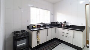 Een kleine keuken met witte kastjes, een zwart aanrecht, een fornuis en een raam met blinds.