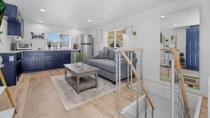 A modern kitchen with dark blue cabinets, a gray sofa, and a wooden coffee table. - Rucker Avenue Cozy Bungalow (Everett)