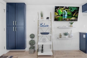 A modern living room with a TV mounted on the wall, a blue wardrobe, a white shelving unit with decorative items, and a small plant. - Rucker Avenue Cozy Bungalow (Everett)