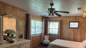 Un dormitorio con cama, cómoda, tocador con espejo, silla y ventilador de techo.