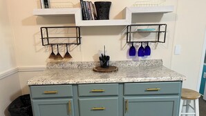 Una cocina con armarios azul claro, una encimera de granito y una pared blanca. Hay dos repisas sobre la encimera, una con libros y la otra con un botellero que contiene dos vasos azules.