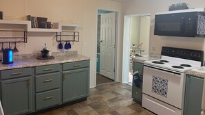 Una cocina con estufa blanca, microondas y pileta. Hay alacenas y una encimera.