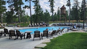 Zona de piscina con sillones de descanso y mesas, rodeada de árboles y una estructura de madera.