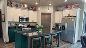 Una cocina con armarios blancos, una isla central con taburetes de bar, un refrigerador de acero inoxidable y un microondas.