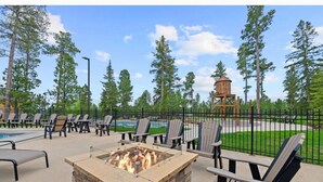 Un patio al aire libre con un hogar a leña de piedra, sillas Adirondack y una piscina.