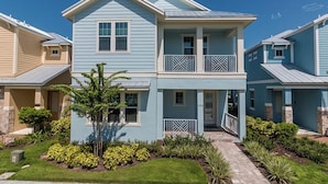 A two-story residential building with a balcony on the second floor, a front entrance, and a well-maintained garden with various plants.