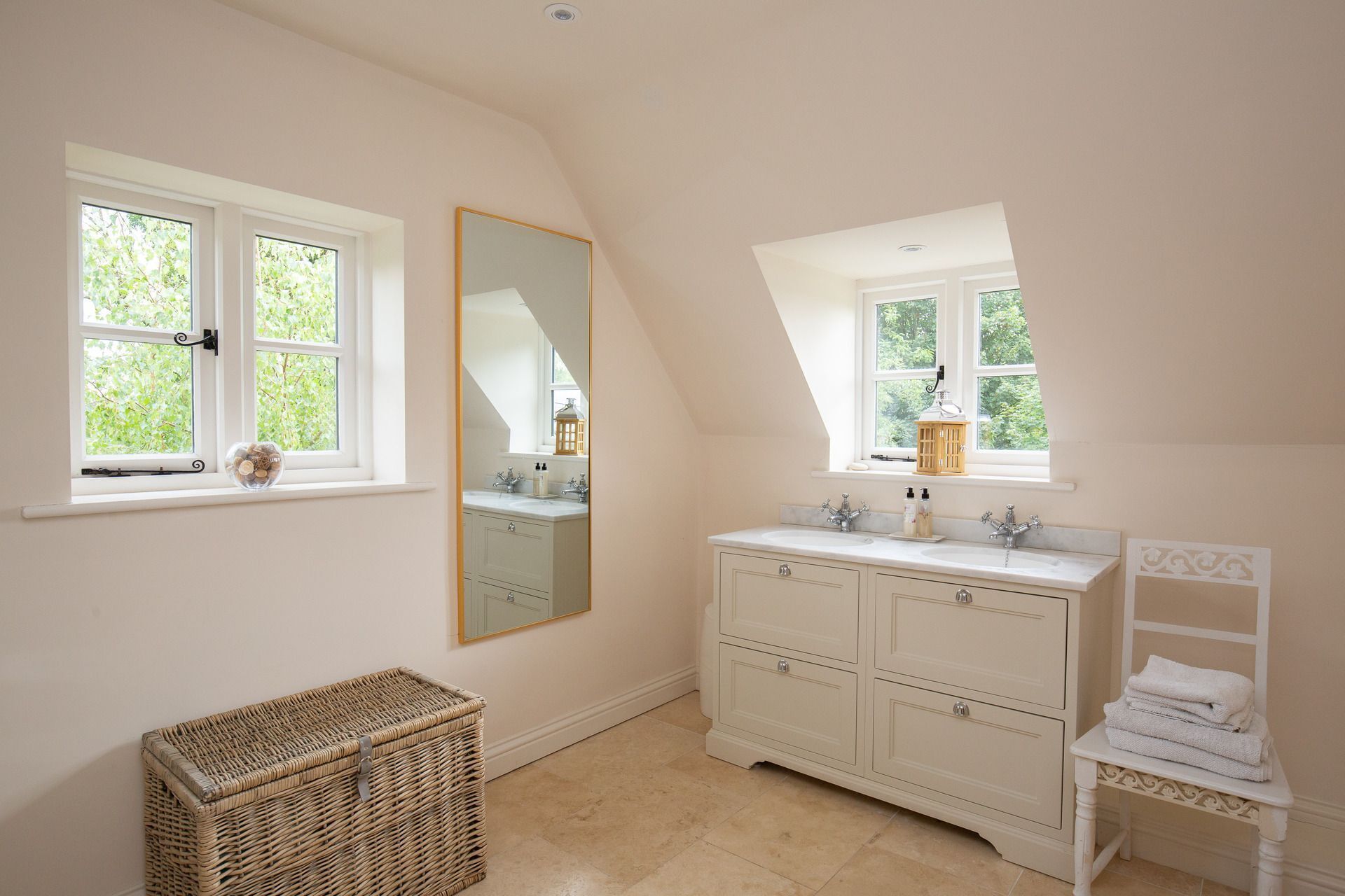 A bathroom with a large mirror, a white vanity, and a window with a view of greenery.