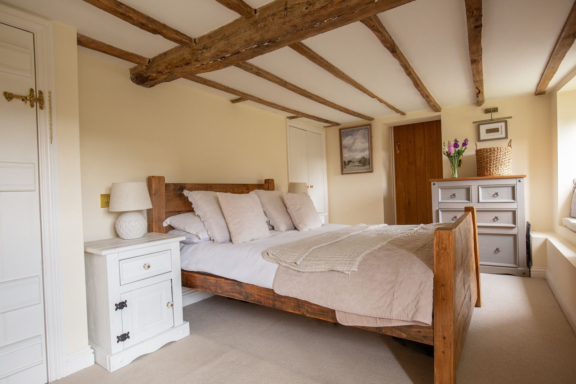 Una camera da letto con un letto in legno, comodini bianchi, una cassettiera e travi a vista in legno.