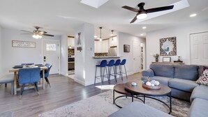A spacious living area with a dining table, blue chairs, a gray sofa, and a ceiling fan.