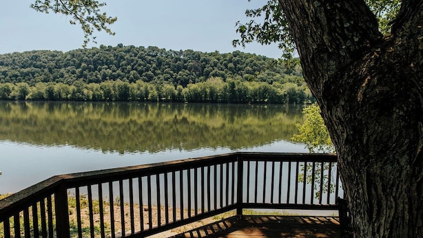 Terraza de madera con barandilla que da a un lago tranquilo, rodeada de un bosque denso.