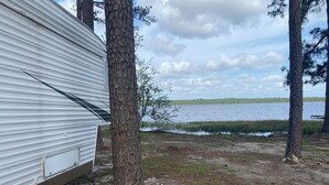A campsite with a trailer, trees, and a lake. - Lakeside 2-bedroom RV in charming Hartsville with AC, WiFi (Hartsville)