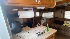 A compact RV kitchen with wooden cabinets, a sink, and a coffee maker. - Lakeside 2-bedroom RV in charming Hartsville with AC, WiFi (Hartsville)