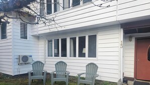 Een huis met twee stoelen op de veranda, een rode deur en een raam met luiken.