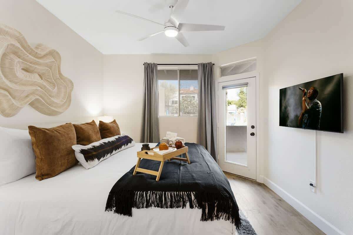 A bedroom with a bed, a ceiling fan, a TV, and a window with curtains.