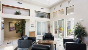 A spacious lobby with a high ceiling, multiple seating areas, and large windows allowing natural light.
